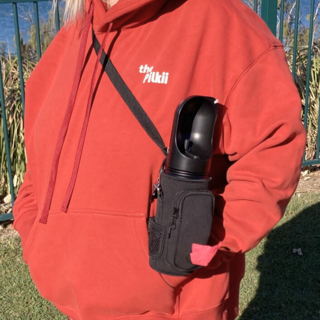 Person wearing a red hoodie with a black dog water bottle as a shoulder bag over their shoulder, standing outdoors.