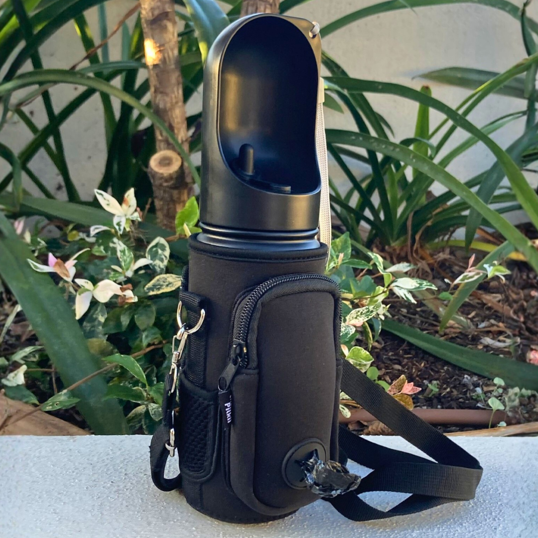 Black pet water bottle with carrying case on a concrete surface with plants in the background