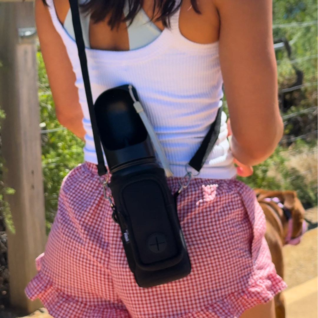 Person wearing a white tank top and pink checkered shorts with a black dog water bottle holder.